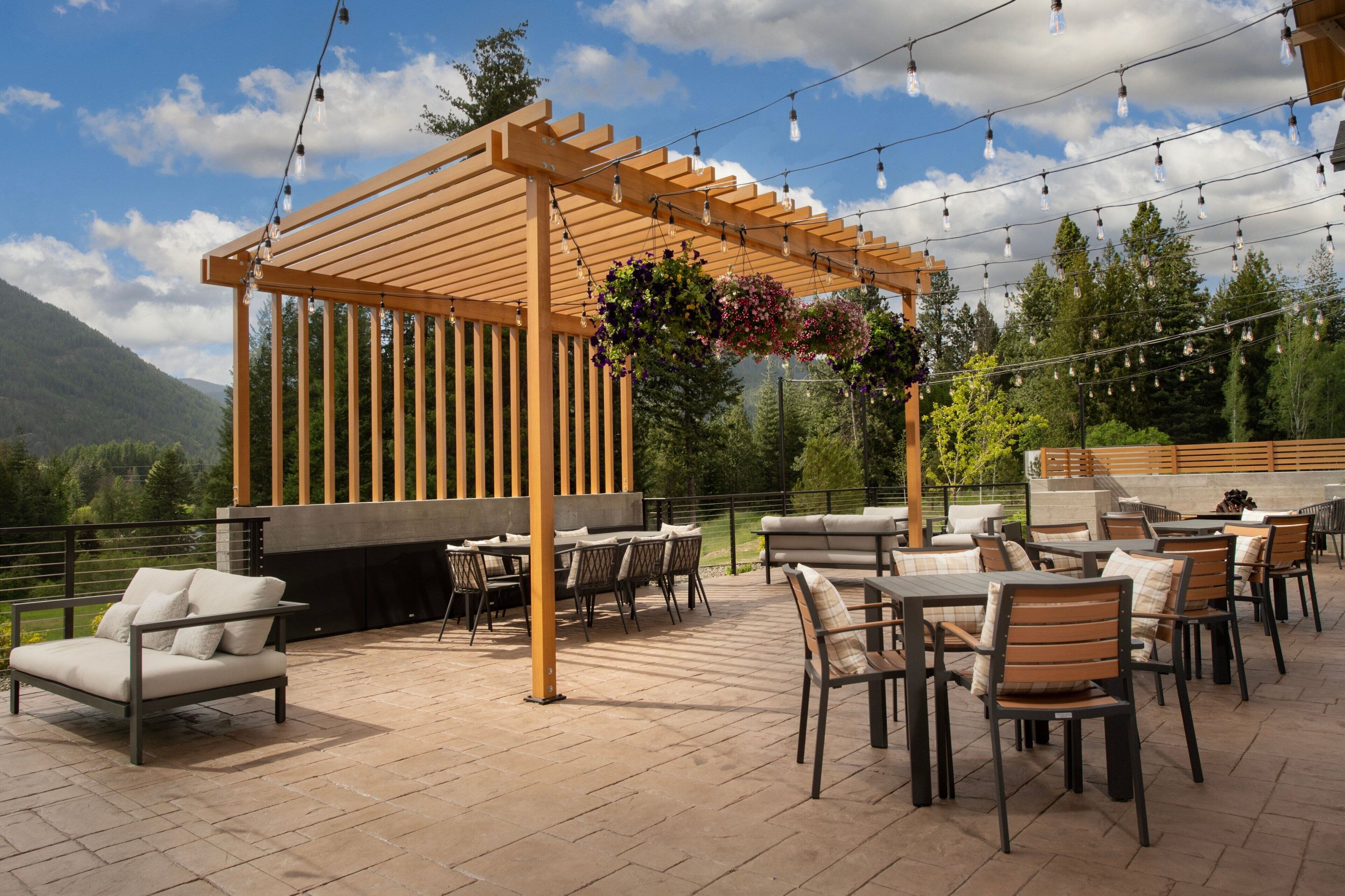Un patio al aire libre con pérgola de madera, luces colgantes y mobiliario exterior.