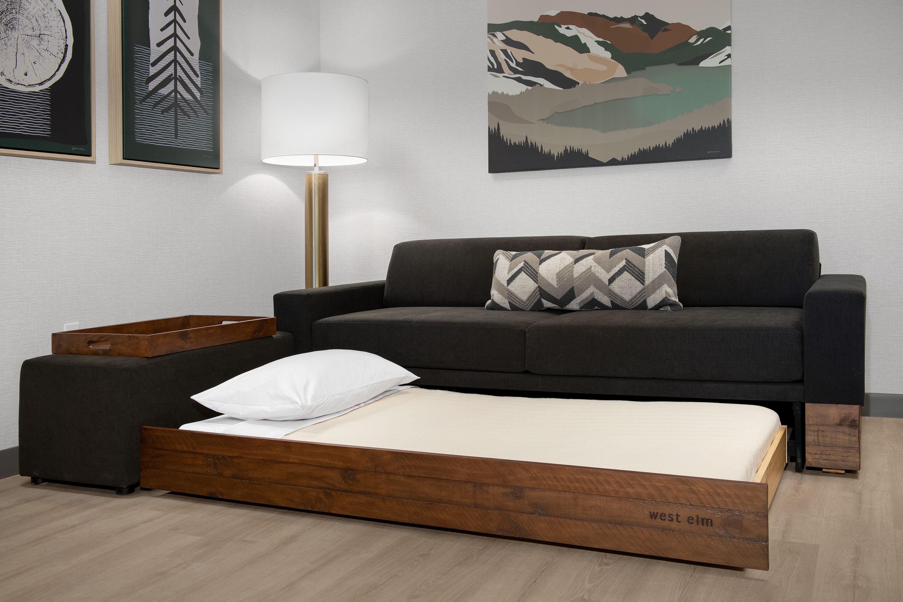 Una habitación moderna con sofá cama, mesita de noche, lámpara y obras de arte en las paredes.