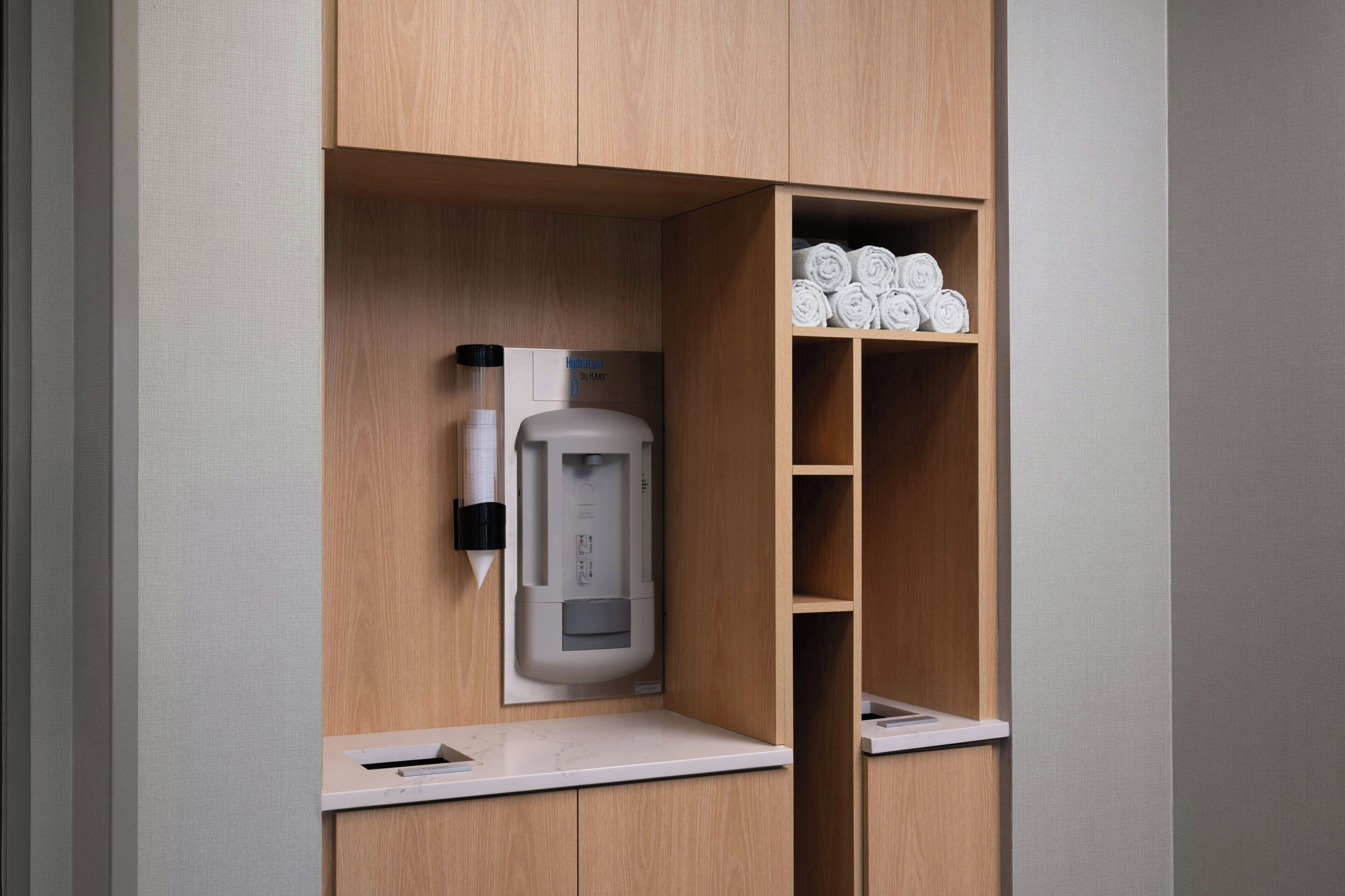 Habitación de hotel con cafetera integrada, un perchero y un estante con toallas cuidadosamente dobladas.