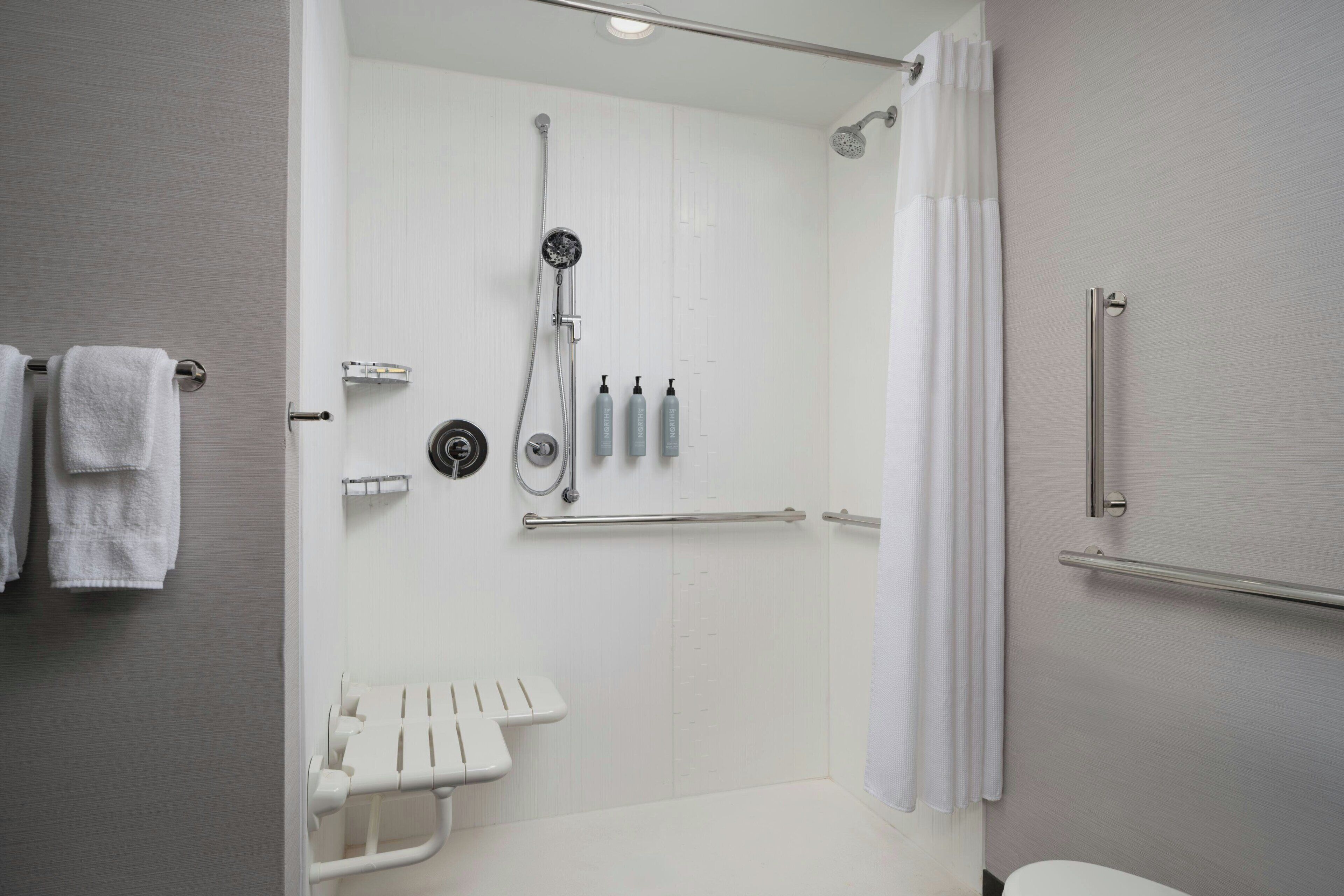 A modern bathroom with a walk-in shower, grab bars, a toilet with a safety seat, and a towel rack.