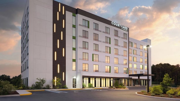 Un hotel de varios pisos con un diseño moderno, que cuenta con una entrada destacada y un área de estacionamiento.