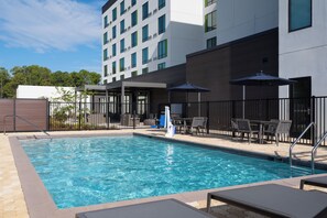 A swimming pool with lounge chairs and umbrellas, surrounded by a fence and a building with multiple windows. - Courtyard By Marriott Lake City (Lake City)