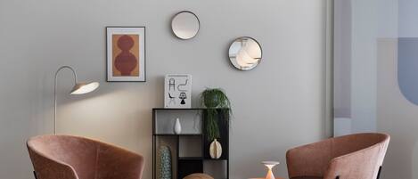 Una sala moderna con dos sillones marrones, una lámpara de pie, una mesita y una estantería con objetos decorativos.