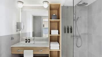 A modern bathroom with a large mirror, a wooden vanity, a shower with a handheld showerhead, and a towel rack.