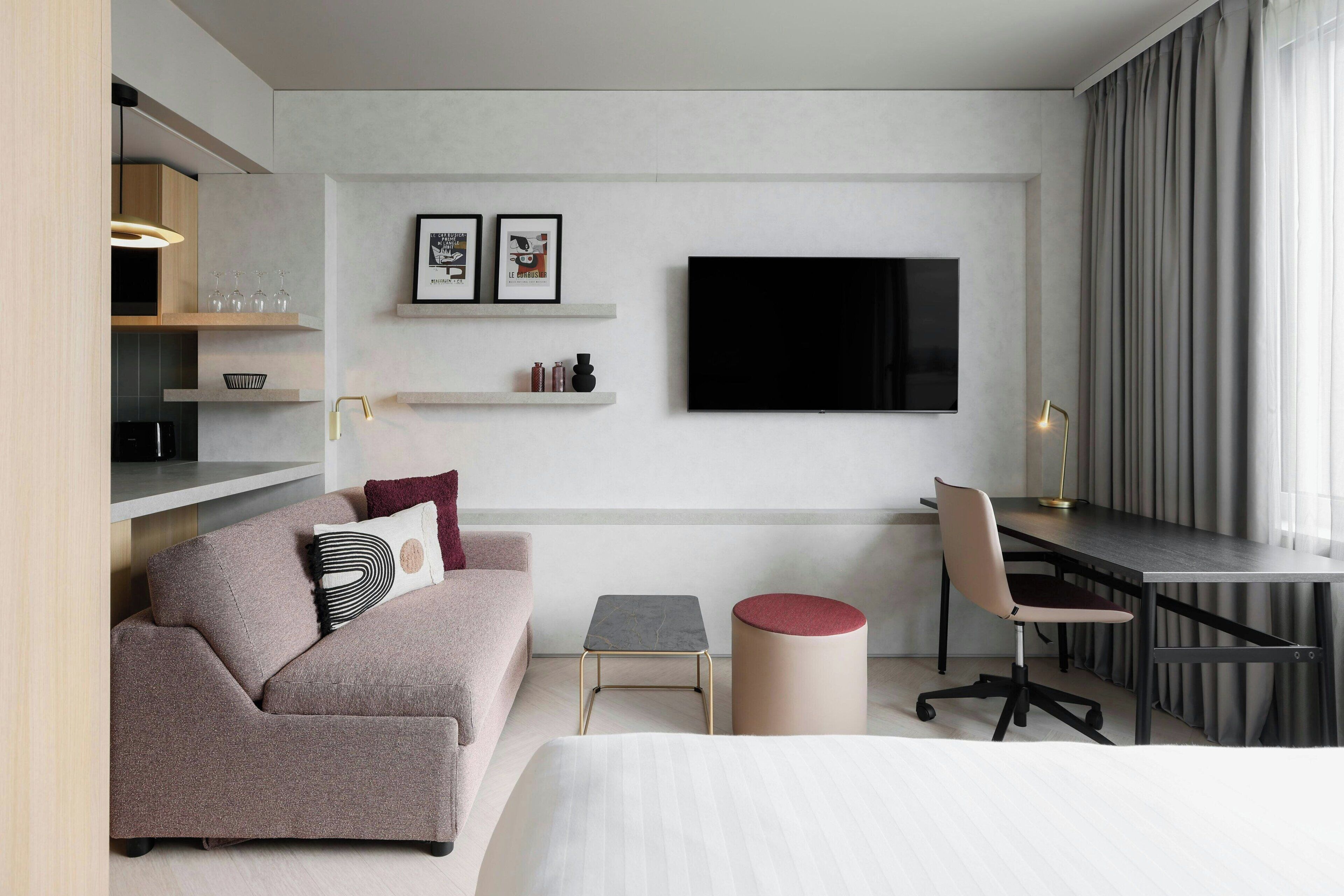 Una habitación de hotel moderna con una cama, un sofá, un escritorio y un televisor.