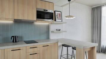 Una cocina moderna con armarios de madera, microondas integrado, hervidor y un taburete de bar.