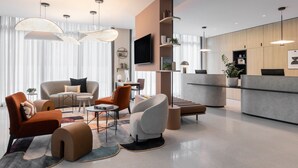 Eine moderne Hotelhalle mit einer Sofagruppe, einem Couchtisch, einem Essbereich und einer Rezeption.