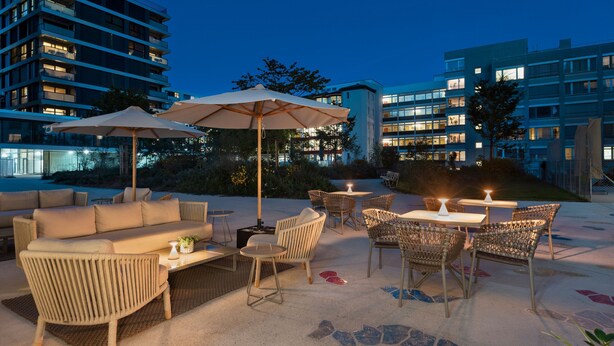 Ein Terrassenbereich mit Sitzgelegenheiten, darunter eine Couch und Stühle, sowie Tische mit Sonnenschirmen.