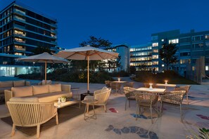 Un espace extérieur aménagé en terrasse, avec des coins salon comprenant un canapé et des fauteuils, ainsi que des tables dotées de parasols.