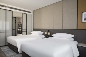 A modern hotel room with two beds, a large mirror, and a neutral color palette.