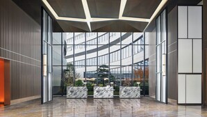A modern lobby with a glass facade, a reception desk, and a geometric ceiling design. - Sheraton Pujiang (Jinhua)