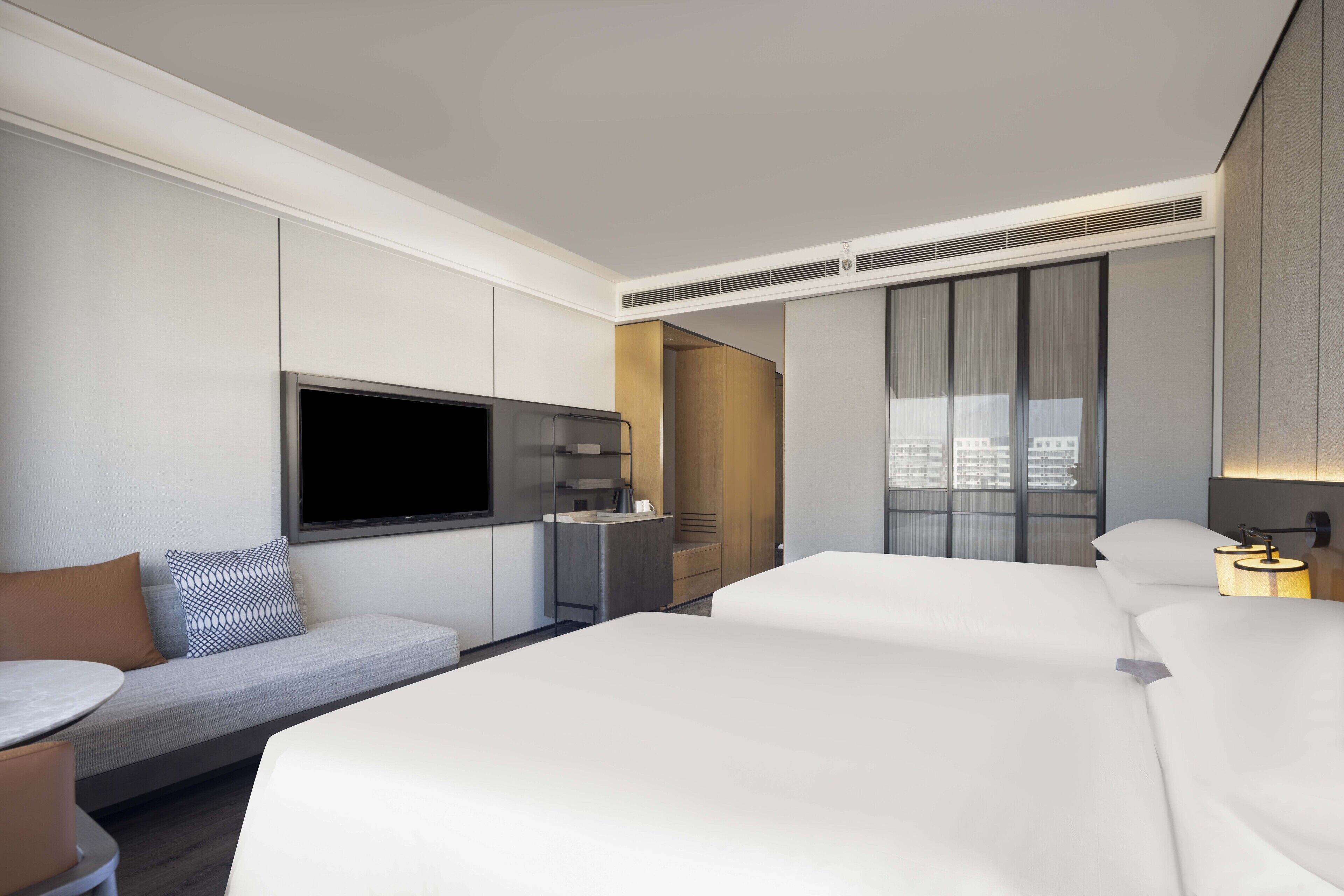 Una habitación de hotel moderna con una cama grande, un sofá, un televisor, un minibar y una ventana con cortinas.