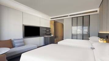 Una habitación de hotel moderna con una cama grande, un sofá, un televisor, un minibar y una ventana con cortinas.