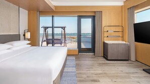 A hotel room with a large bed, a desk, a TV, and a balcony with a view of the city. - Sheraton Pujiang (Jinhua)