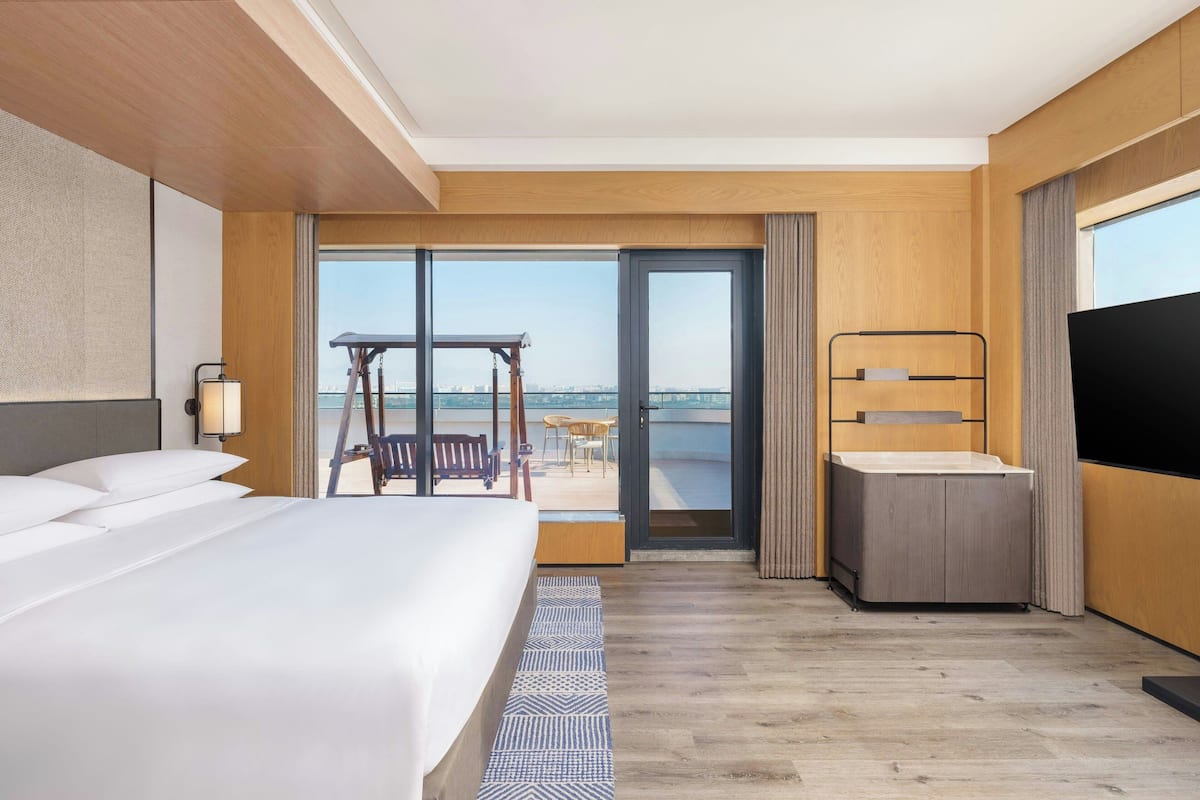 Ein Hotelzimmer mit einem großen Bett, einem Schreibtisch, einem Fernseher und einem Balkon mit Blick auf die Stadt.