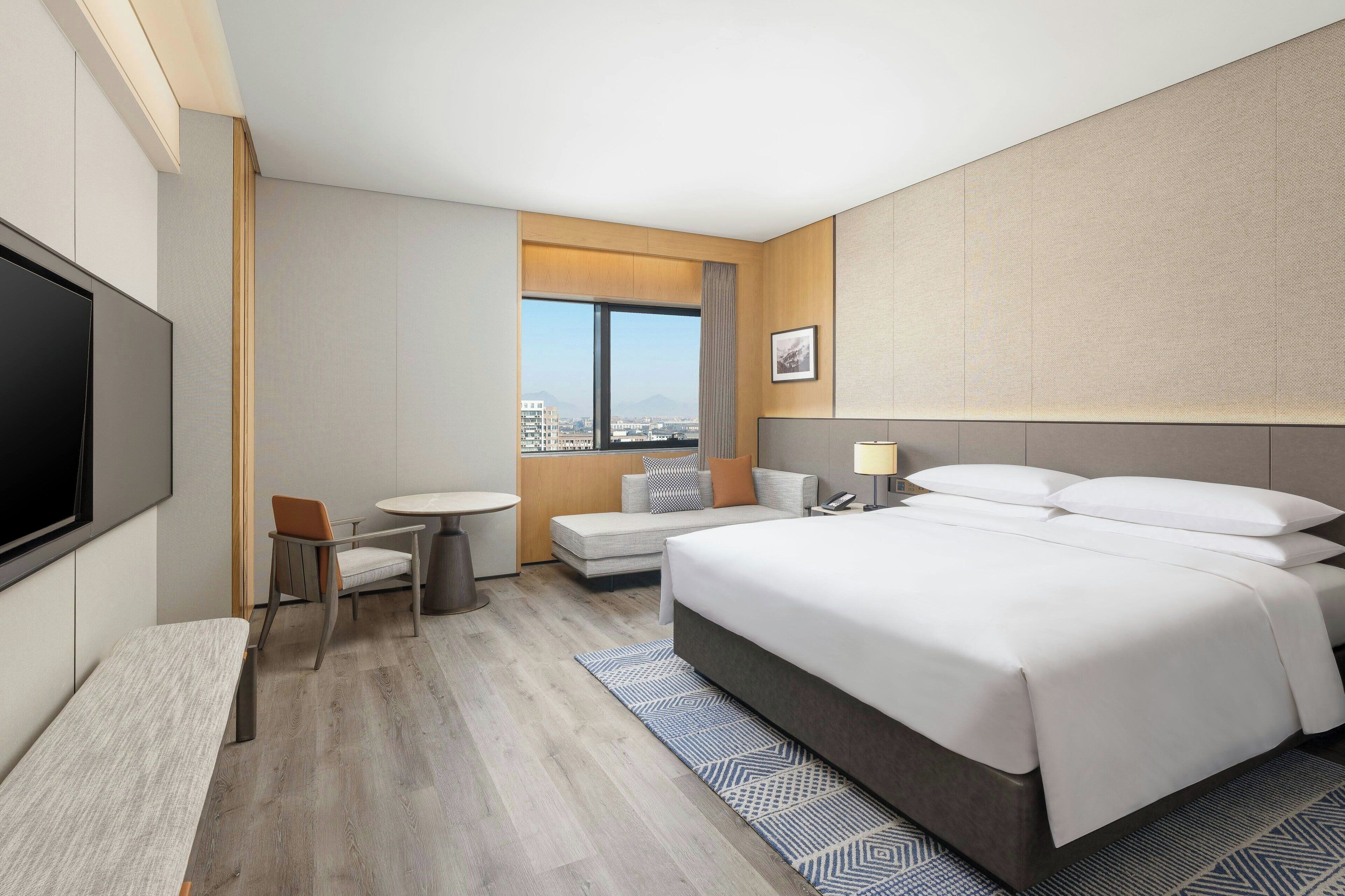 Quarto de hotel com uma cama grande, uma escrivaninha, uma cadeira e uma televisão.