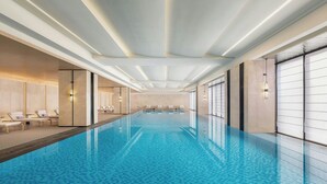 A modern indoor swimming pool with a tiled floor, lounge chairs, and a clean, minimalist design. - Sheraton Pujiang (Jinhua)