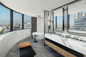 A modern bathroom with a large bathtub, a double sink vanity, and a bench.