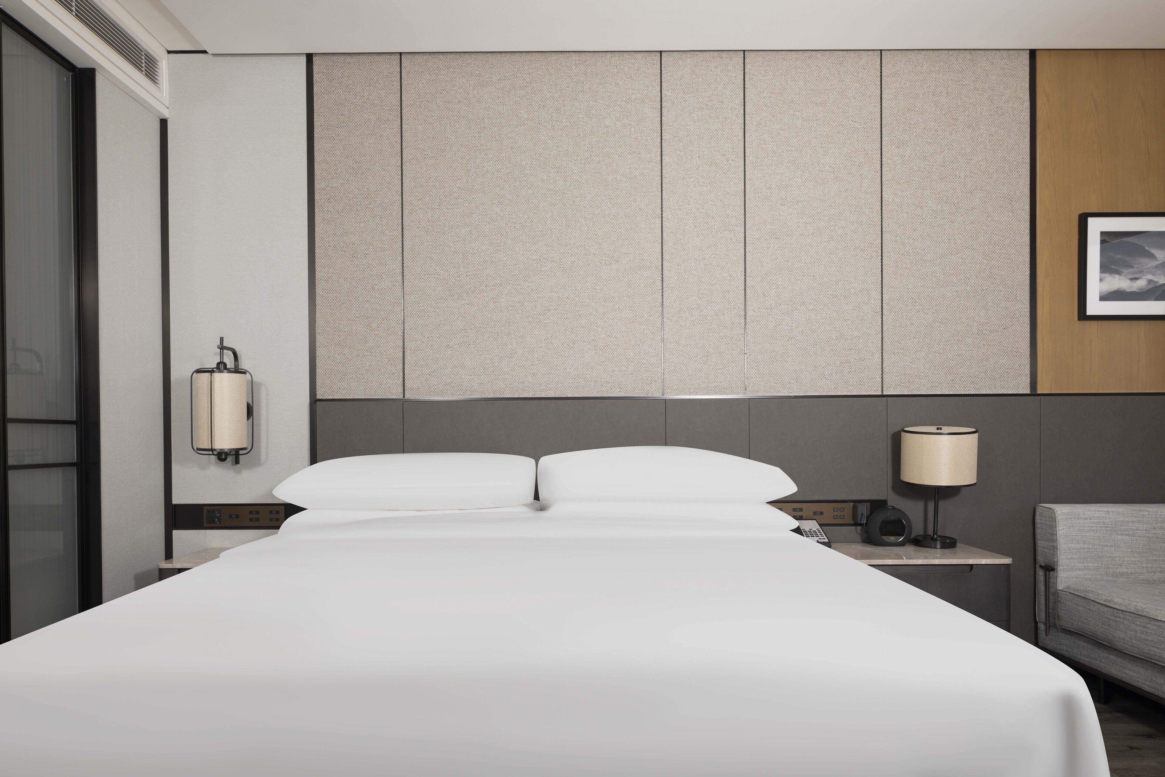 Una habitación de hotel moderna con una cama grande, una mesita de noche con lámpara y vistas a la ciudad.