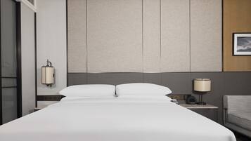 Una habitación de hotel moderna con una cama grande, una mesita de noche con lámpara y vistas a la ciudad.