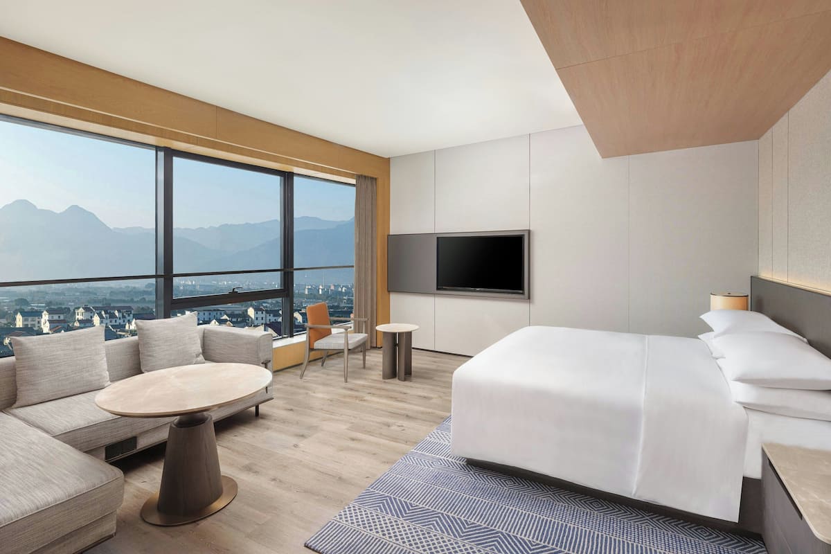 Ein modernes Hotelzimmer mit großem Fenster, einer Couch, einem runden Tisch, einem Bett und einem Fernseher.