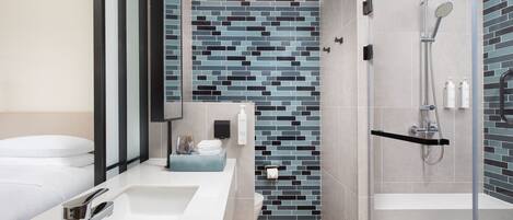 Un baño moderno con cabina de ducha de vidrio, un lavabo blanco y un salpicadero de azulejos.