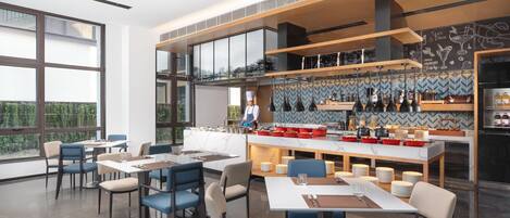 A modern restaurant with a bar area, large windows, and a chef preparing food.