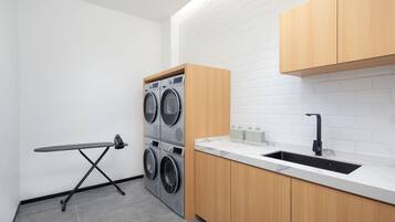 Cocina compacta con lavadora y secadora integradas, una plancha pequeña y un lavamanos con grifo moderno.