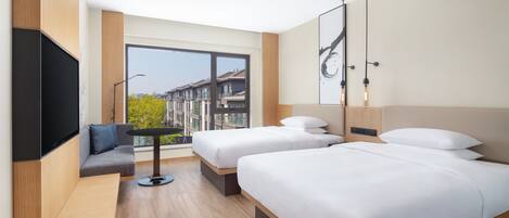 Habitación de hotel con dos camas, un sofá, un televisor y un ventanal con vistas a la ciudad.
