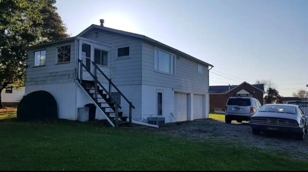 A two-story house with a front staircase, a garage, and a driveway with two cars.