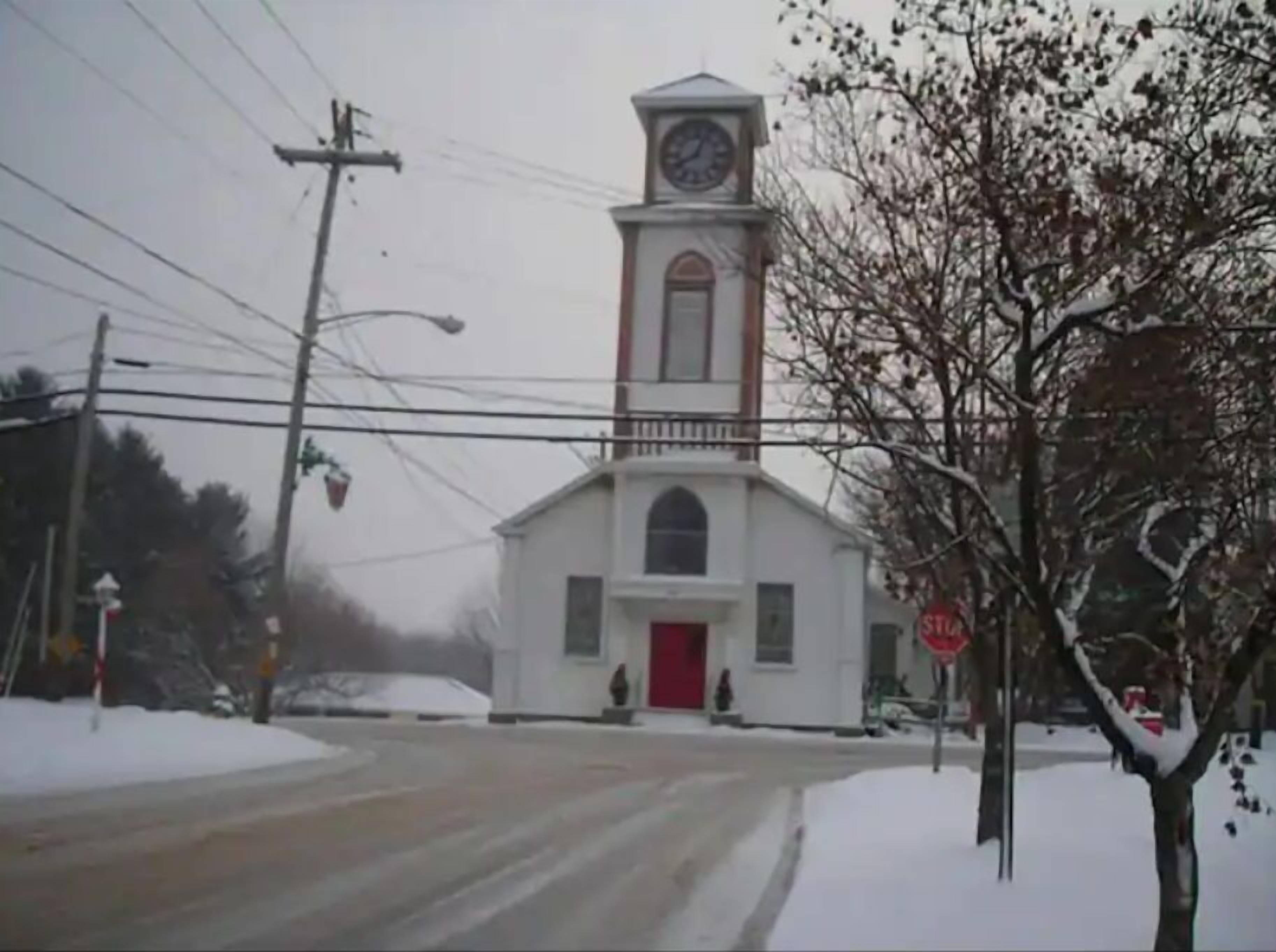A church with a clock tower, a red door, and a snowy environment.