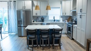 A modern kitchen with white cabinets, a central island with bar stools, stainless steel appliances, and pendant lighting. - Spacious Smoky Mountain Retreat in Sevierville (Sevierville)