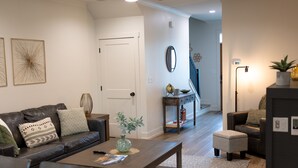 A modern living room with a dark leather sofa, a wooden coffee table, and a dining area with a white table and bar stools. - Spacious Smoky Mountain Retreat in Sevierville (Sevierville)