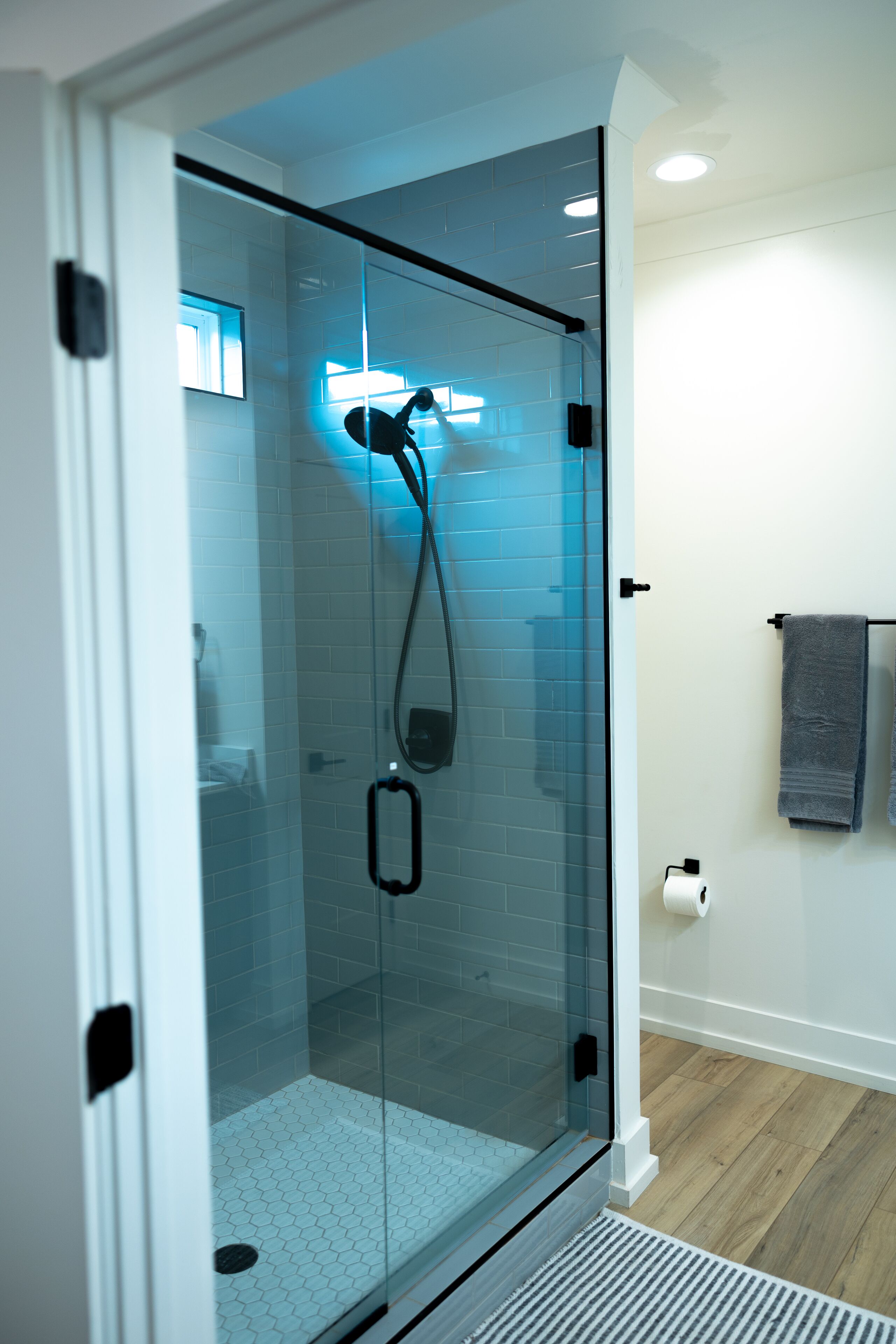 Un baño moderno con ducha de vidrio, paredes de azulejos blancos y suelo de madera.