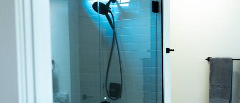 Un baño moderno con ducha de vidrio, paredes de azulejos blancos y suelo de madera.