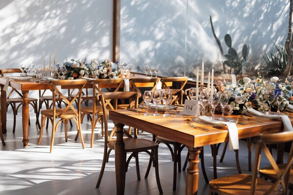 Un comedor con mesas y sillas de madera, cada conjunto con copas de vino, platos y velas.
