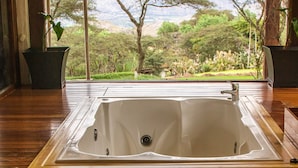 Ein Zimmer mit Holzboden, einer großen rechteckigen Badewanne und Blick auf eine natürliche Landschaft durch große Fenster.