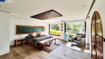 A bedroom with a large bed, a bedside table, a bench, a chair, and a view of a garden through a large window.