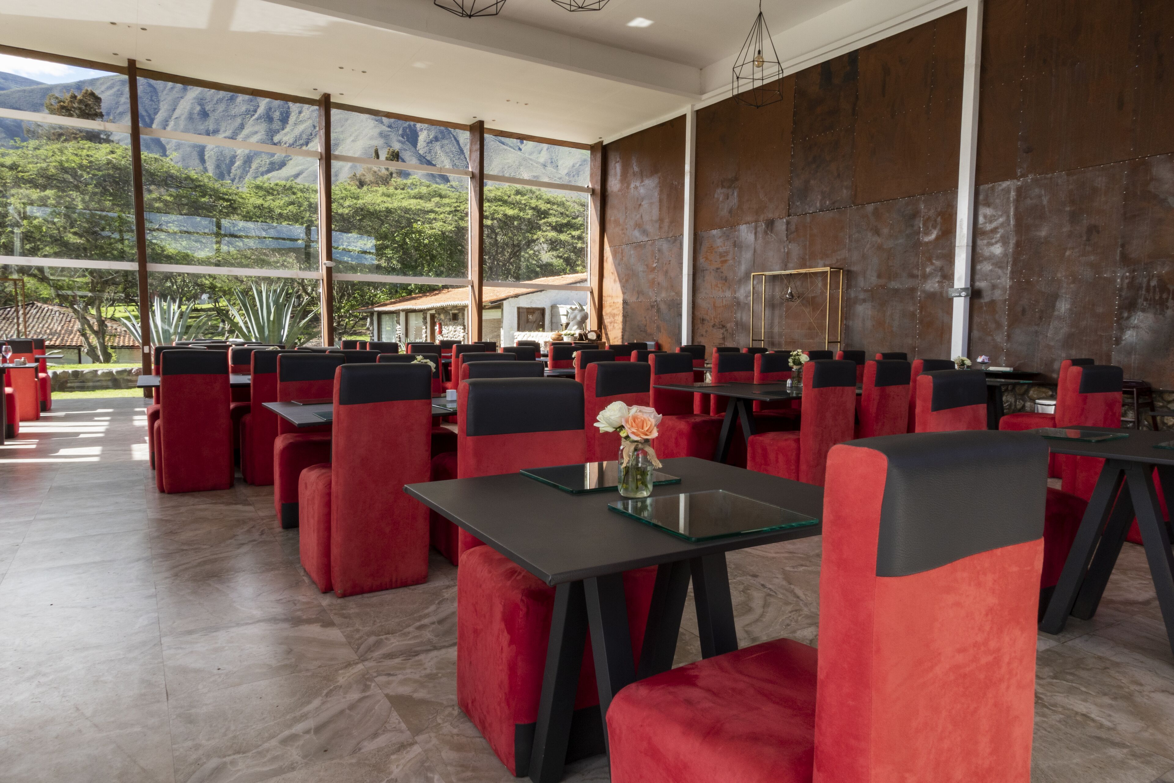 Un restaurante con sillas rojas y negras, grandes ventanales y vistas a las montañas.