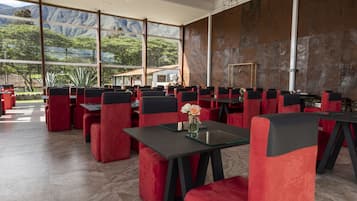 Un restaurante con sillas rojas y negras, grandes ventanales y vistas a las montañas.