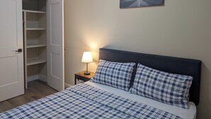 A bedroom with a bed, a nightstand with a lamp, a painting on the wall, and a wardrobe.