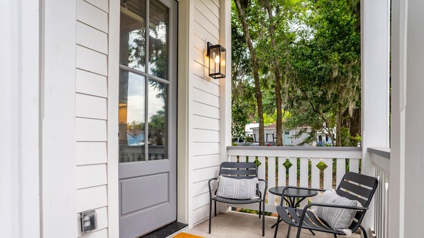 A porch with two chairs and a small table, a door, and a window with a view of trees and a house. - Cara May Cottage  (Beaufort)
