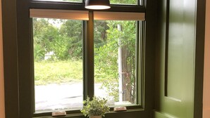 A green-painted room with a bench and a table under a window, a potted plant, and a hanging light fixture. - Cara May Cottage  (Beaufort)