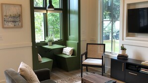 A cozy living room with a green accent wall, a dining area with a bench, a comfortable sofa, a TV, and a bookshelf. - Cara May Cottage  (Beaufort)