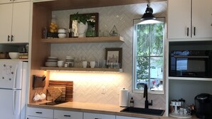 A modern kitchen with white cabinetry, a wooden countertop, a built-in oven, and a window with a view of greenery. - Cara May Cottage  (Beaufort)