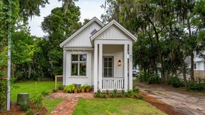A small, single-story house with a white exterior, a front porch, and a brick pathway leading to the entrance. - Cara May Cottage  (Beaufort)