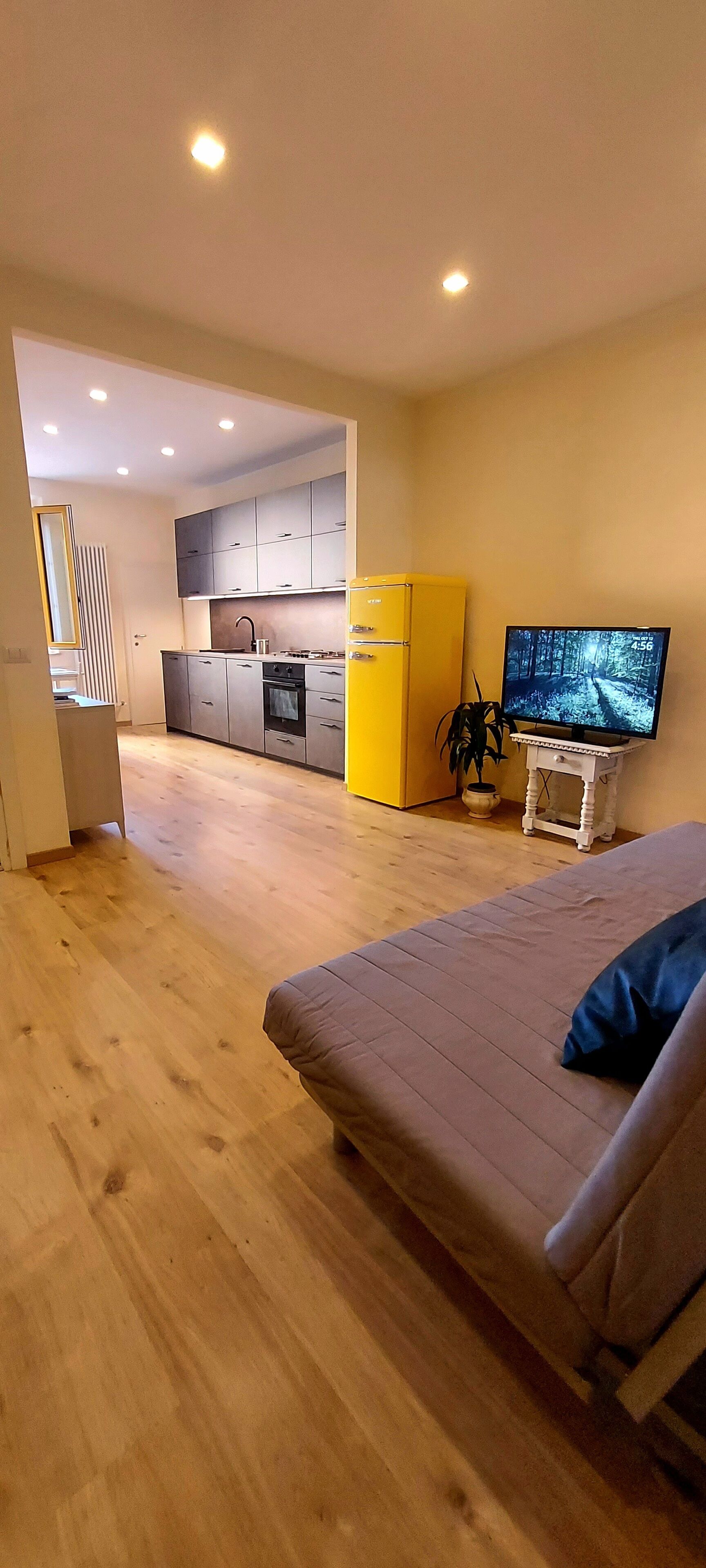 Een modern appartement met houten vloer, een bank, een televisie, een keuken met kastjes en een gele koelkast.
