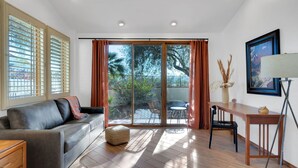 A modern living room with a sofa, a coffee table, a desk, and a sliding glass door leading to an outdoor area with a patio table and chairs. - Fun-for-all! Pool! Private Pickleball Court! Game room! (Tucson)