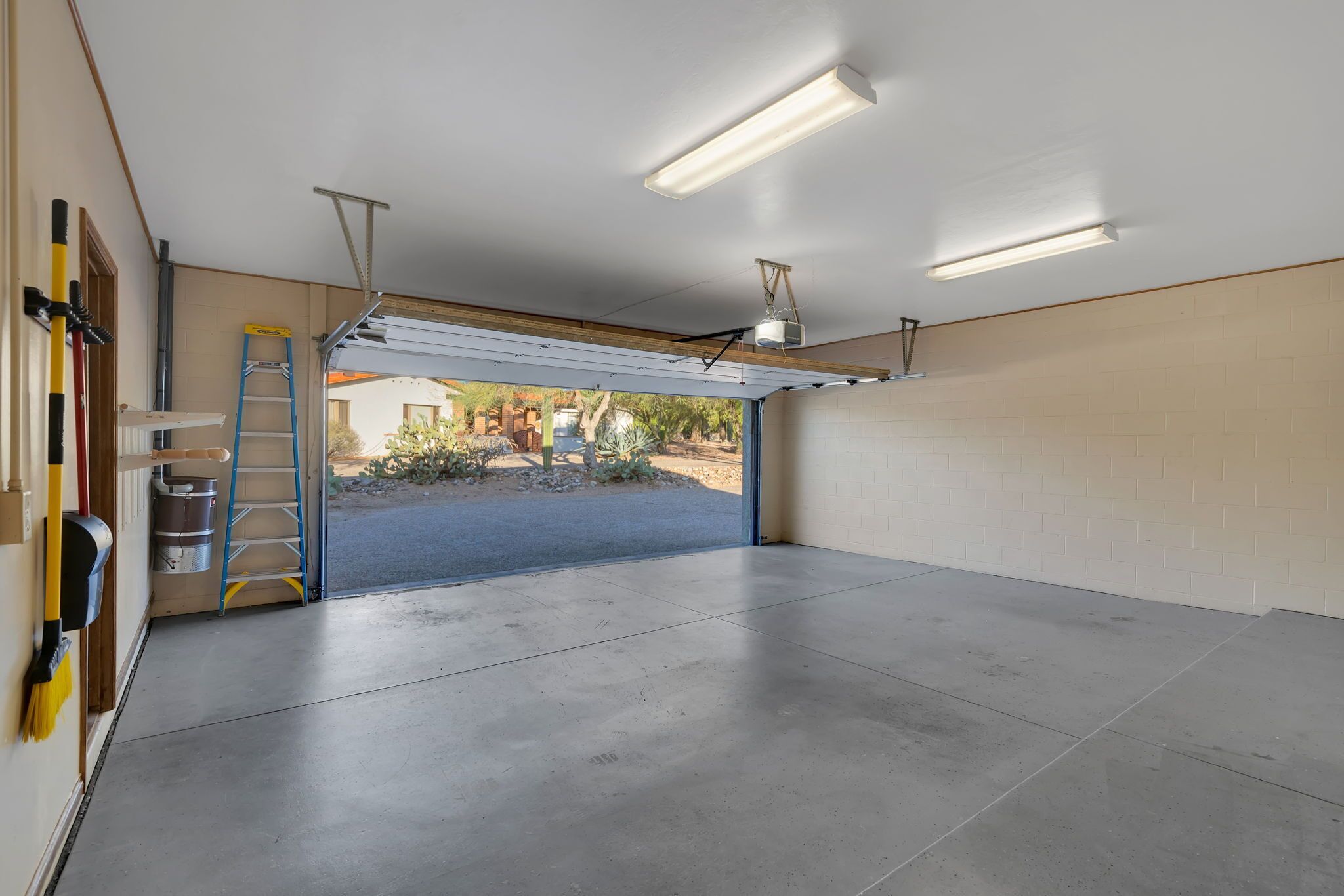 A garage with a concrete floor, a blue ladder, and a partially open garage door.