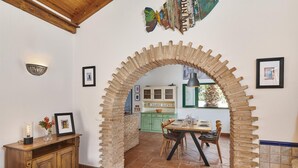 A dining area with a rustic brick archway, wooden furniture, and a view into a kitchen with green cabinets. - Charming Rural Retreat, A/C, Private Pool & Beautiful Views - 11km from the Coastal Town of Tavira! (Tavira)